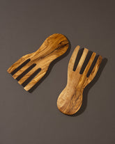 A pair of flat olivewood serving forks placed on a dark surface.
